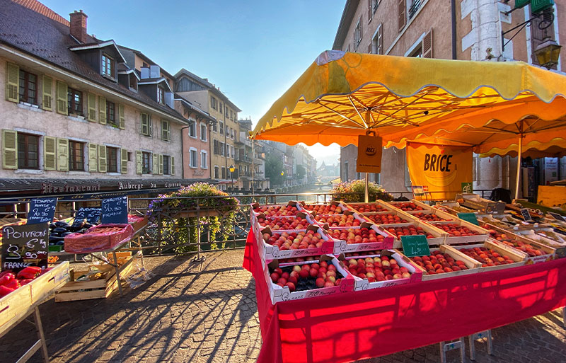 Puesto de frutas en un mercado sobre un puente adoquinado sobre un canal en Annecy