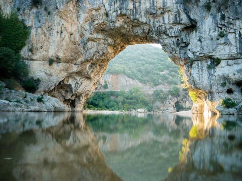 Aguas tranquilas fluyen debajo de un puente de roca formado naturalmente en el desfiladero de Ardèche