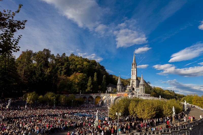 Una enorme plaza llena de gente en Lourdes en Francia con las agujas de las iglesias al fondo