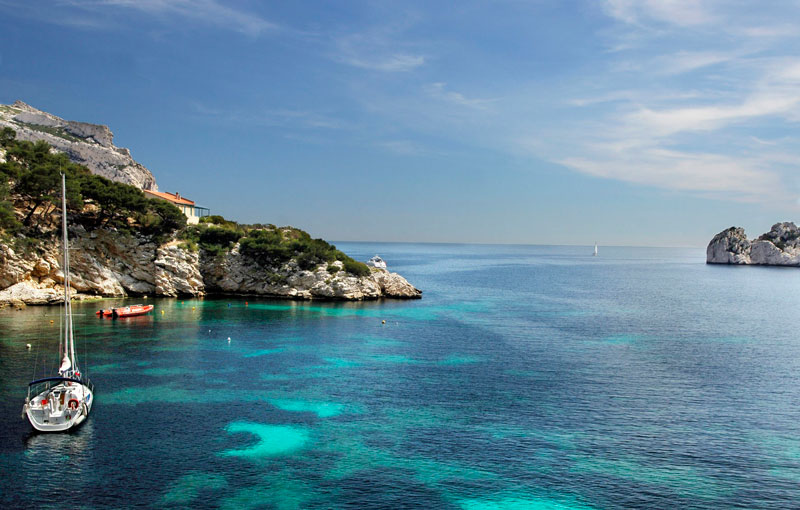 Aguas claras del Mediterráneo frente a la costa de la ciudad de Marsella, pequeñas embarcaciones flotando y colinas rocosas bordean un puerto natural