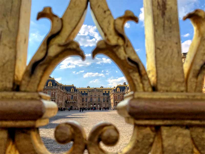 Vista del palacio de Versalles a través de puertas doradas a través de un gran patio adoquinado
