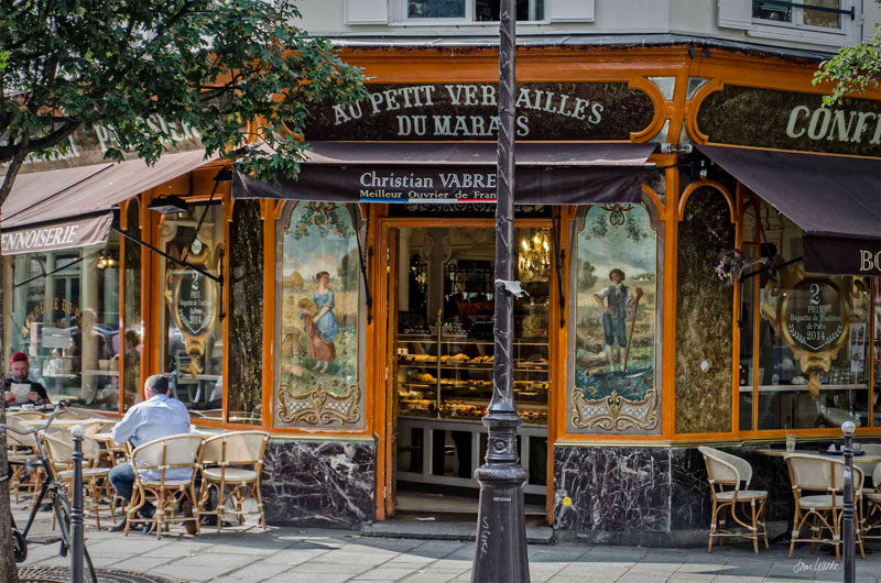 Hermosa panadería en París con frente de azulejos, gente sentada en mesas enfrente disfrutando de café y croissants