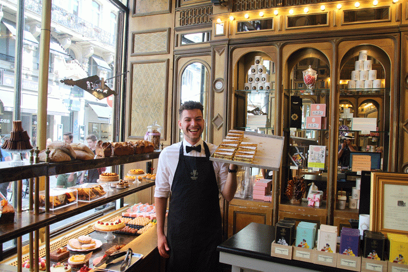 El hombre sostiene una bandeja de deliciosos pasteles en una pastelería antigua en Lille