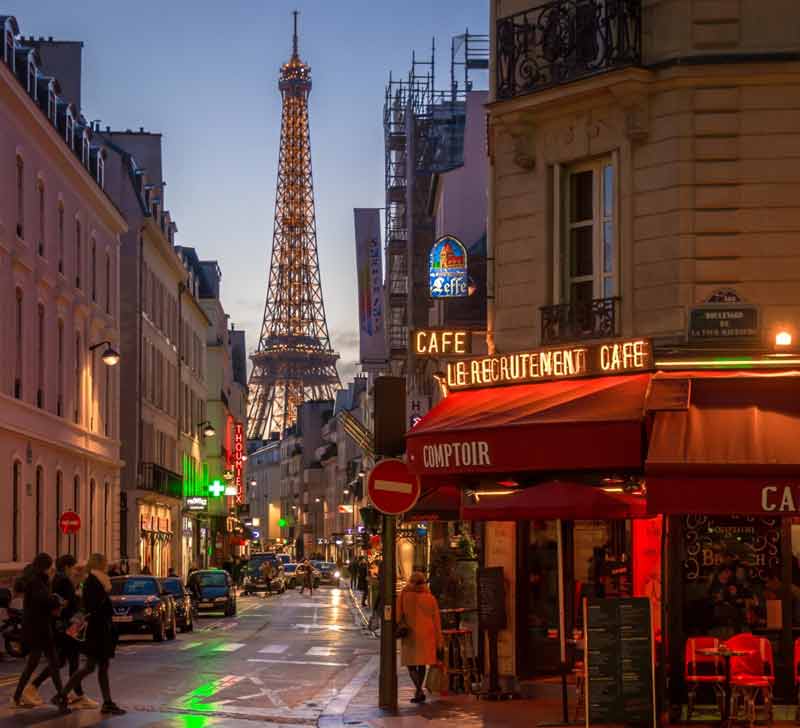 Torre Eiffel al atardecer fotografiada desde una calle lateral llena de bares y tiendas